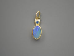 14K and sterling silver backing pendant with a blue oval boulder opal and a blue Montana sapphire set at the top in a star shape. On gray background.