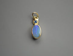 14K and sterling silver backing pendant with a blue oval boulder opal and a blue Montana sapphire set at the top in a star shape. On gray background.