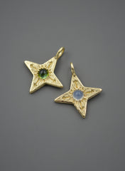 two 14k yellow gold four pointed compass star pendants. One on the left has an olive green cabochon which is tourmaline and the right has a light milky blue chalcedony.