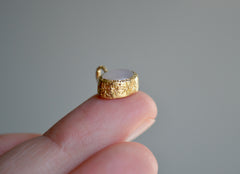 Oval Moonstone set in a textured yellow gold bezel pendant with stars carved into the sides. Side view shown on finger.