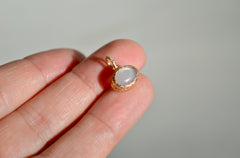 Oval Moonstone set in a textured yellow gold bezel pendant with stars carved into the sides. Shown in sunlight on fingertips.