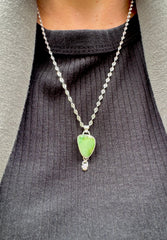 Silver Pendant and Chain with a Green Royston turquoise stone that is an angular shape and a small star dangling element at the bottom with a pink sapphire in the center. Being worn with a black striped shirt and green cardigan.