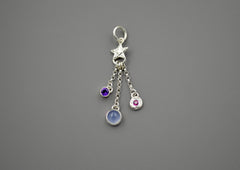 Silver charm featuring a small silver star with 3 separate chain pieces hanging from the bottom. Each has a different gemstone at the end. Purple amethyst, blue chalcedony and berry colored rhodolite garnet.