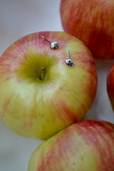 14k gold and sterling silver ladybug pendant laying on a red and green colored apple with other apples surrounding