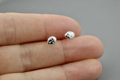 Silver ladybug stud earrings being held between fingers