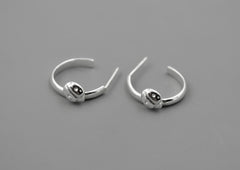 Mismatching ladybug hoop earrings in sterling silver laying on a gray background