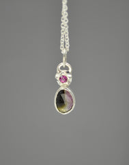 Silver pendant with star element at the top that has a berry pink rhodolite garnet set in the center of it. Underneath is a rose cut bi color tourmaline stone in a bezel setting. The tourmaline has both dark green and baby pink colors in it.