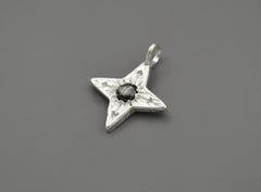 Silver Compass Star Pendant with textured surface and arrows. In the center is a black star sapphire. The "star" appears in direct sunlight.